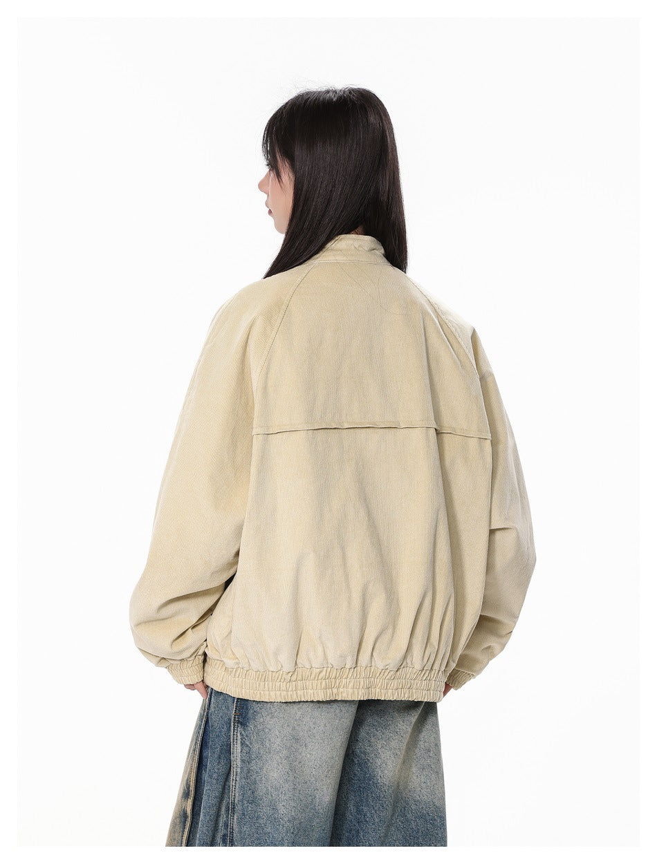 Rear view of a model wearing a beige jacket with a stand collar, raglan sleeves, back yoke, and gathered hem.