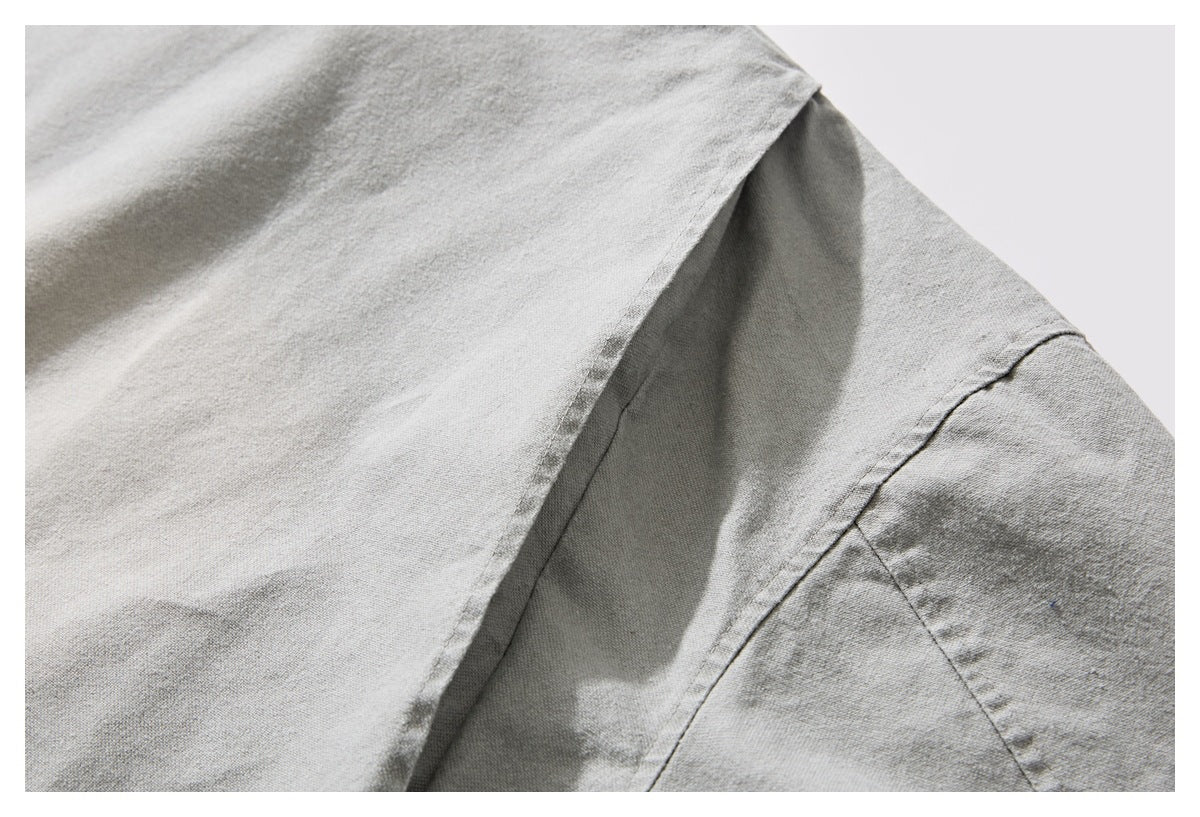 Close-up of light gray garment fabric showing a folded seam and stitching.