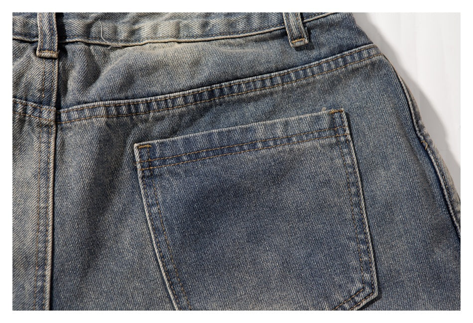 Close-up of a back pocket and yoke stitching on faded blue-gray jeans.