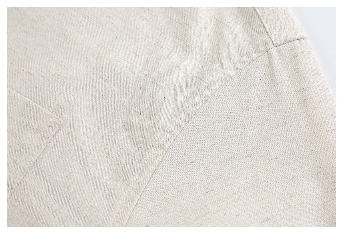 Close-up of ivory flecked garment fabric with intersecting stitched seams and a small pocket edge.