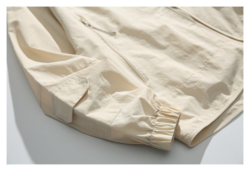 Close-up of a light beige jacket sleeve showing a gathered elastic cuff, flap tab, and zipper.