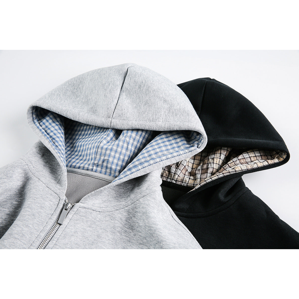 Close-up of gray and black zip-up hoodies with contrasting plaid-lined hoods.