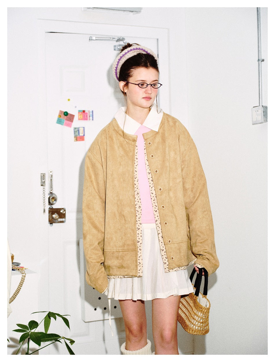 Model in a tan button-front jacket with floral edging, a pink top, and a white skirt, shown at an angle.