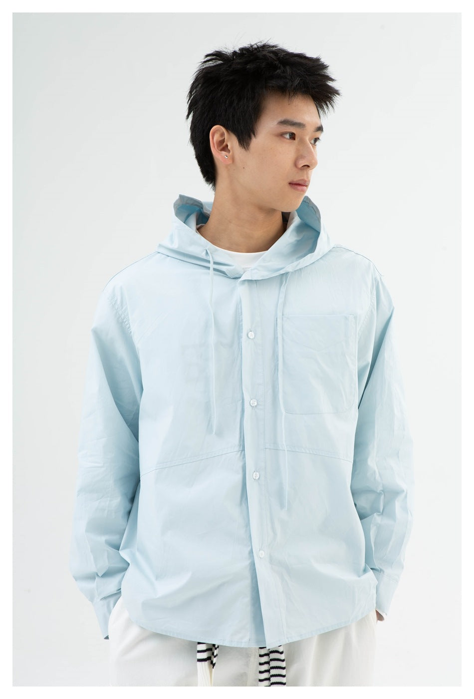 Close view of a model wearing a pale blue hooded shirt with drawstrings, buttons, and a chest pocket.