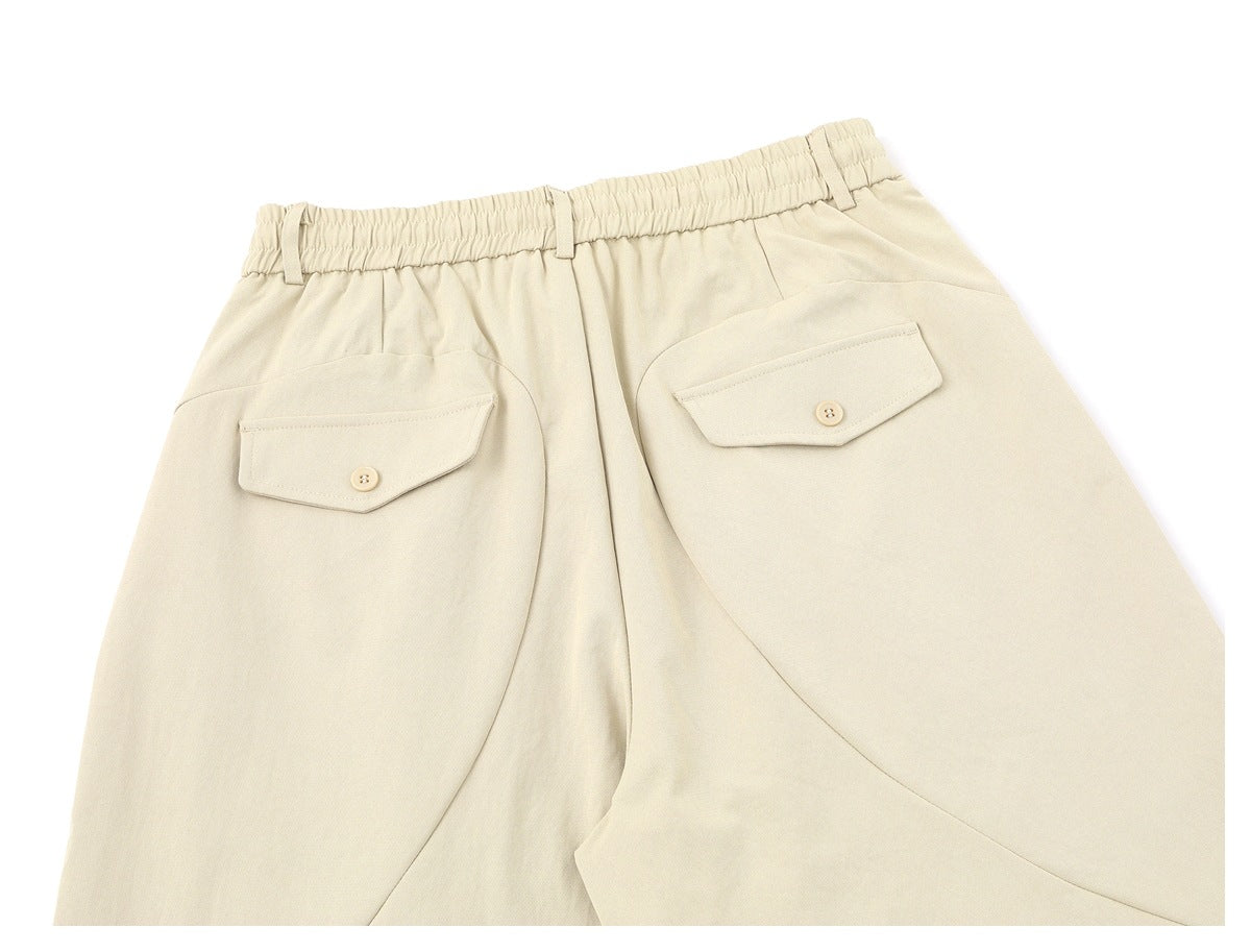 Cropped rear view of cream trousers with an elastic waistband, belt loops, and buttoned flap back pockets.