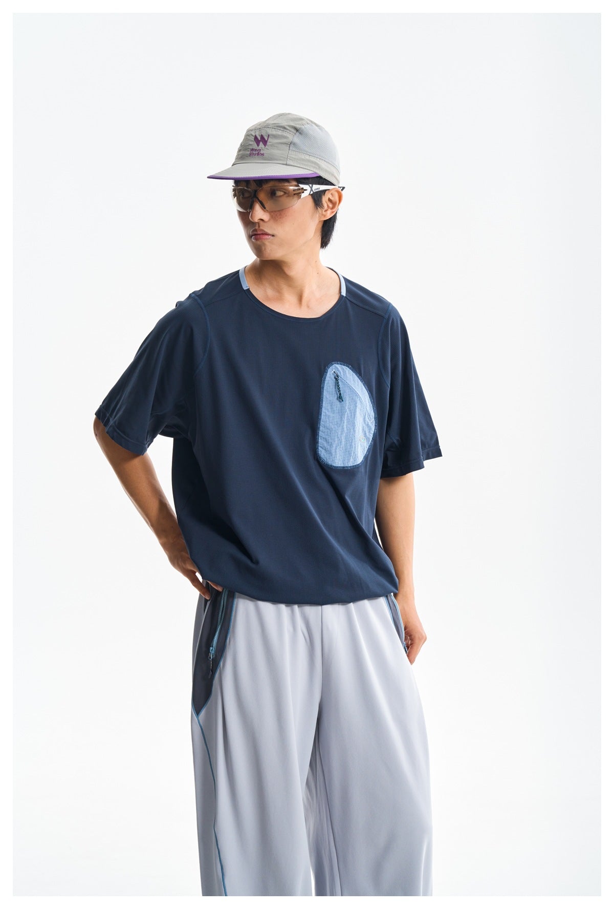 Model in a navy short-sleeve shirt with a light blue chest pocket and light gray pants, shown from the waist up.