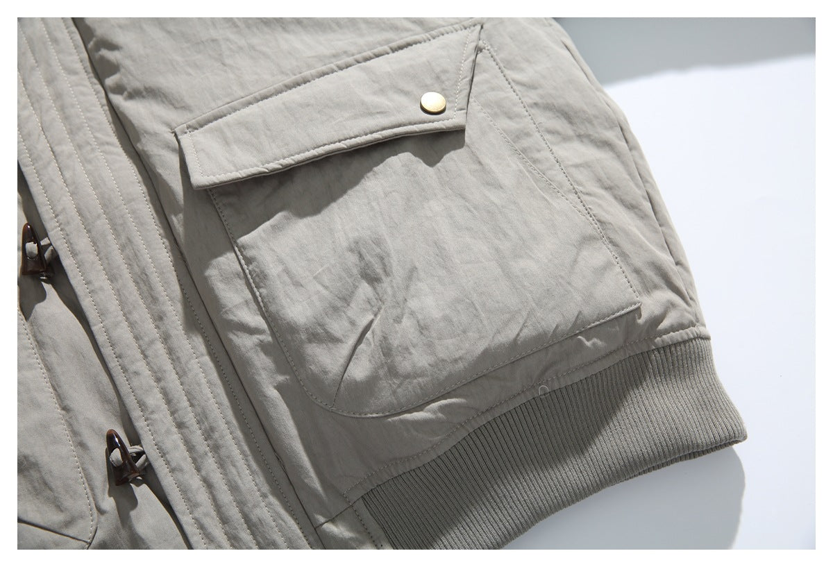 Close-up of a large flap pocket with a brass-colored snap above the taupe jacket's ribbed hem.