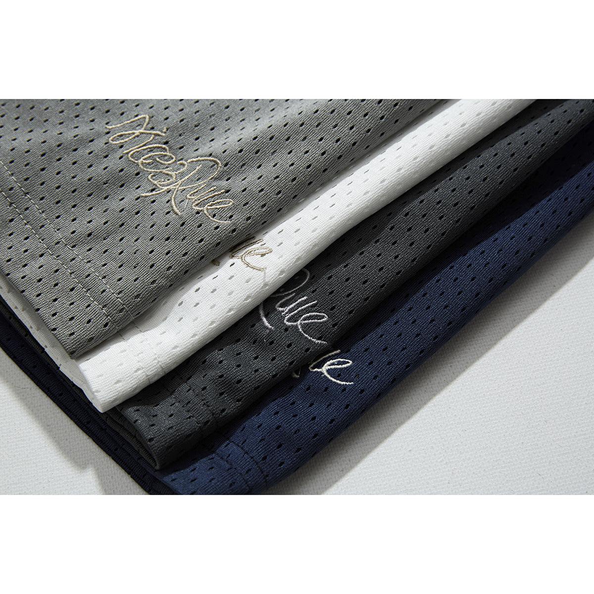 Close-up of perforated mesh shorts in gray, white, black, and navy with small embroidered script logos.