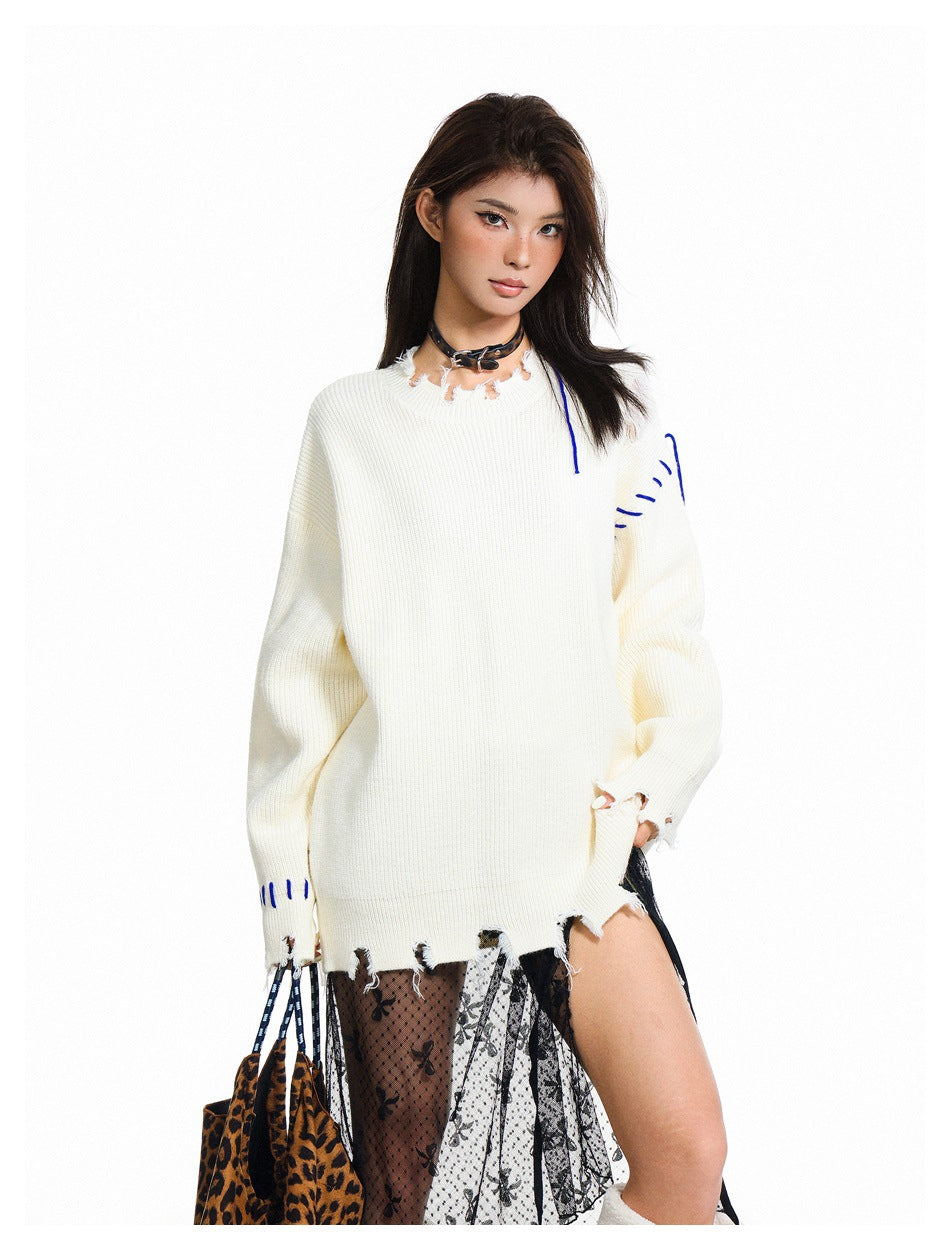 Closer view of a model in an oversized ivory sweater with blue stitch accents and a distressed neckline and hem.