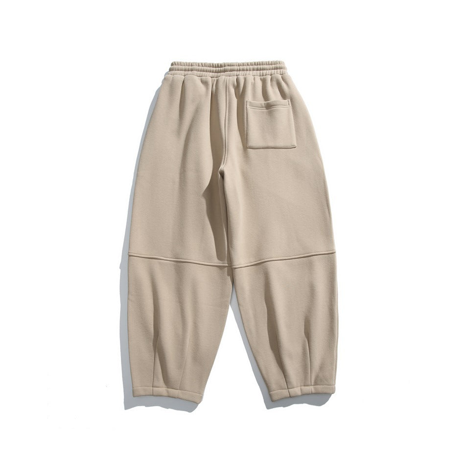 Back view of beige relaxed-fit joggers with an elastic waistband, rear patch pocket and paneled legs.