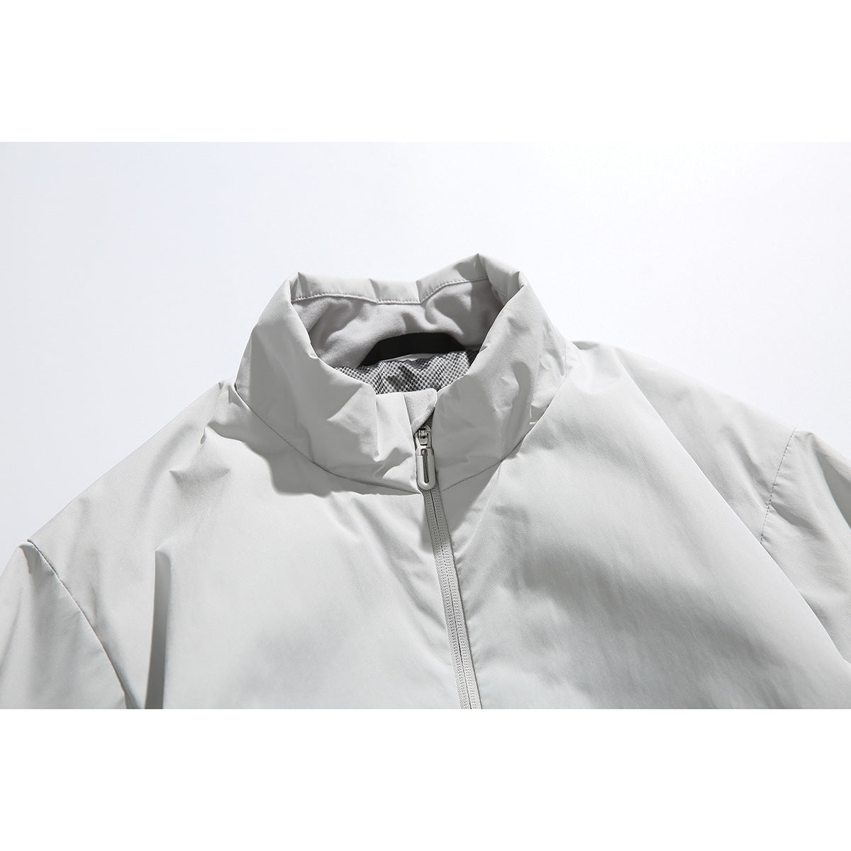Close-up of a light gray jacket's high collar, mesh lining, and central zipper.