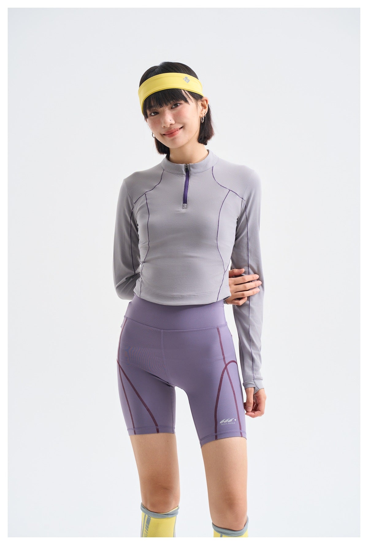 Front view of a model in a light gray-lavender long-sleeve quarter-zip top and purple fitted shorts.
