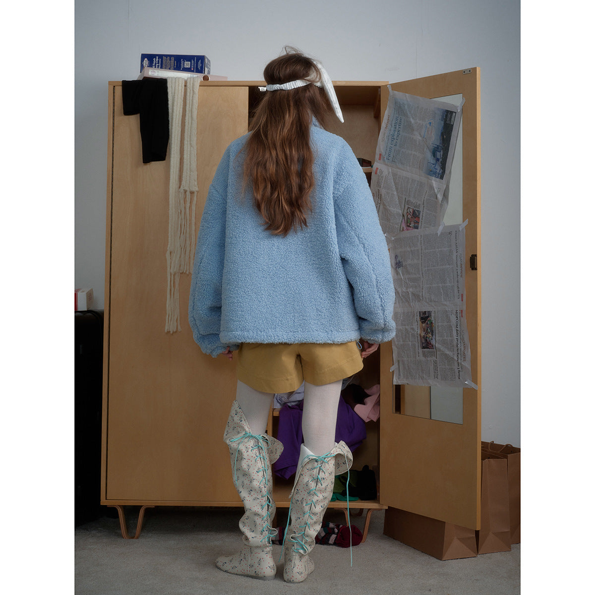 Back view of a model wearing a plain light blue plush jacket with a high collar.