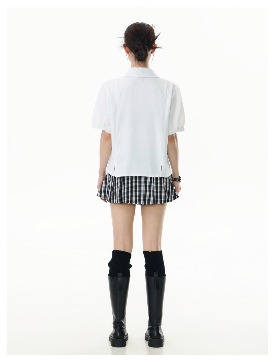 Rear view of a model wearing a white short-sleeve collared shirt with a black-and-white plaid skirt and tall black boots.