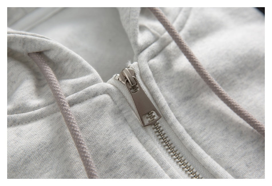 Close-up of a metal zipper and muted gray drawstrings on a light gray heathered hooded garment.