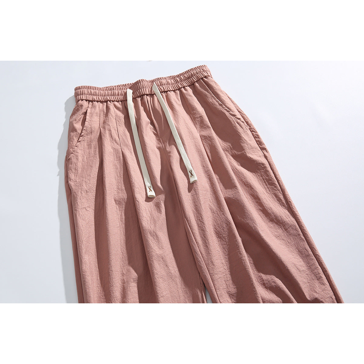 Angled close view of dusty rose wide-leg pants with an elastic waist and long cream drawstrings.