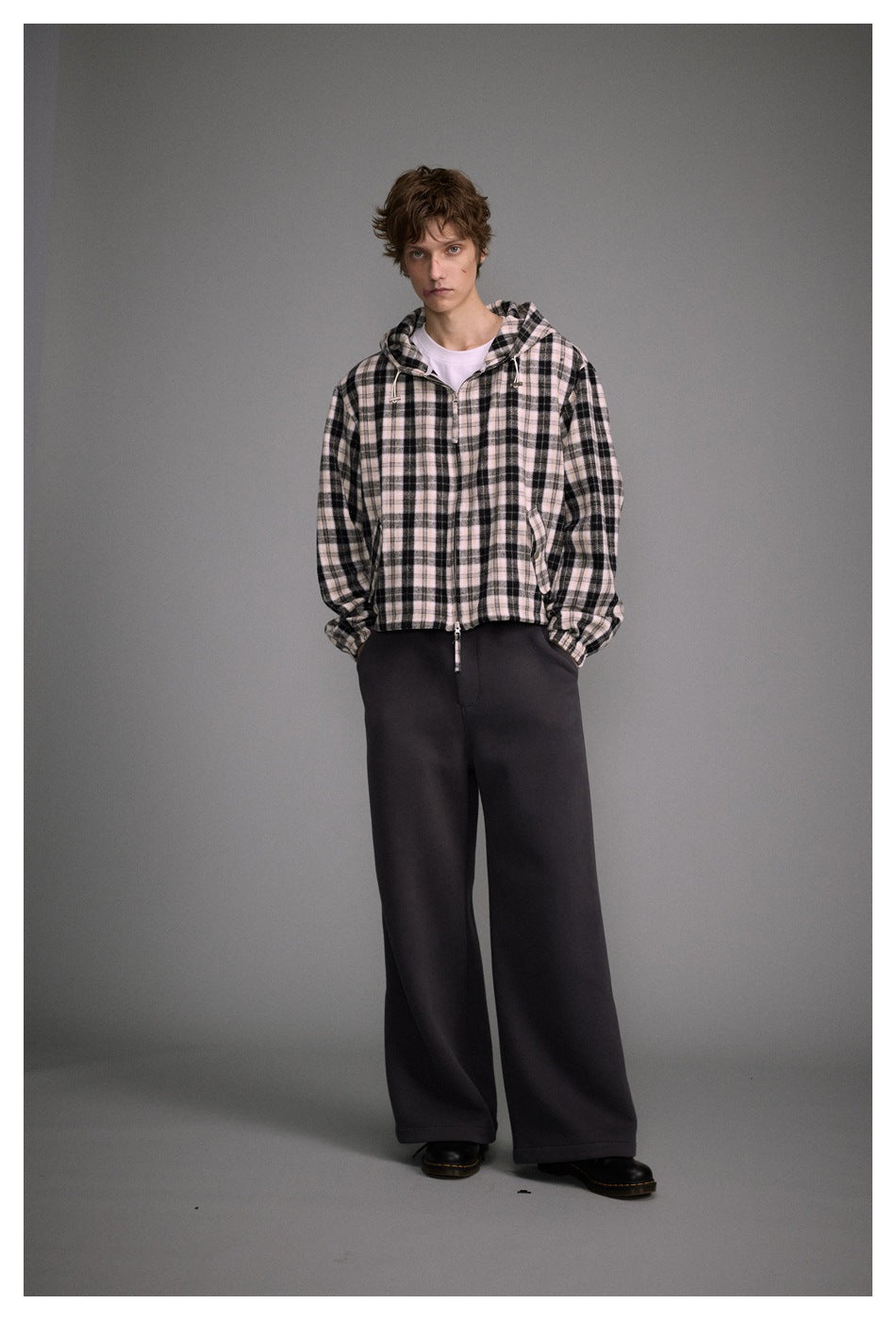 Model wearing a black and pale pink plaid zip-front hooded jacket with black wide-leg trousers.