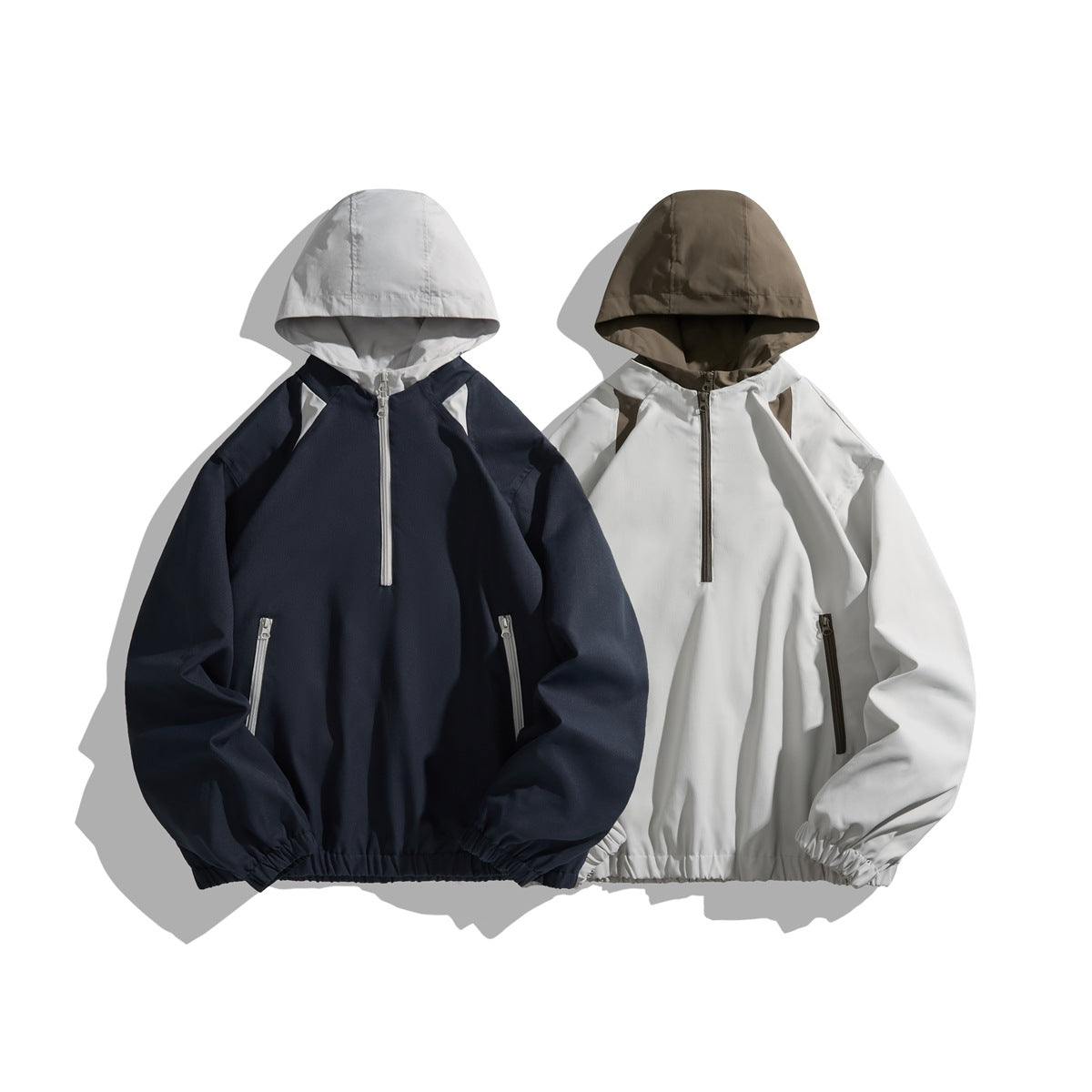 Two hooded half-zip jackets shown from the front: navy with a light gray hood and white accents, and white with a brown hood