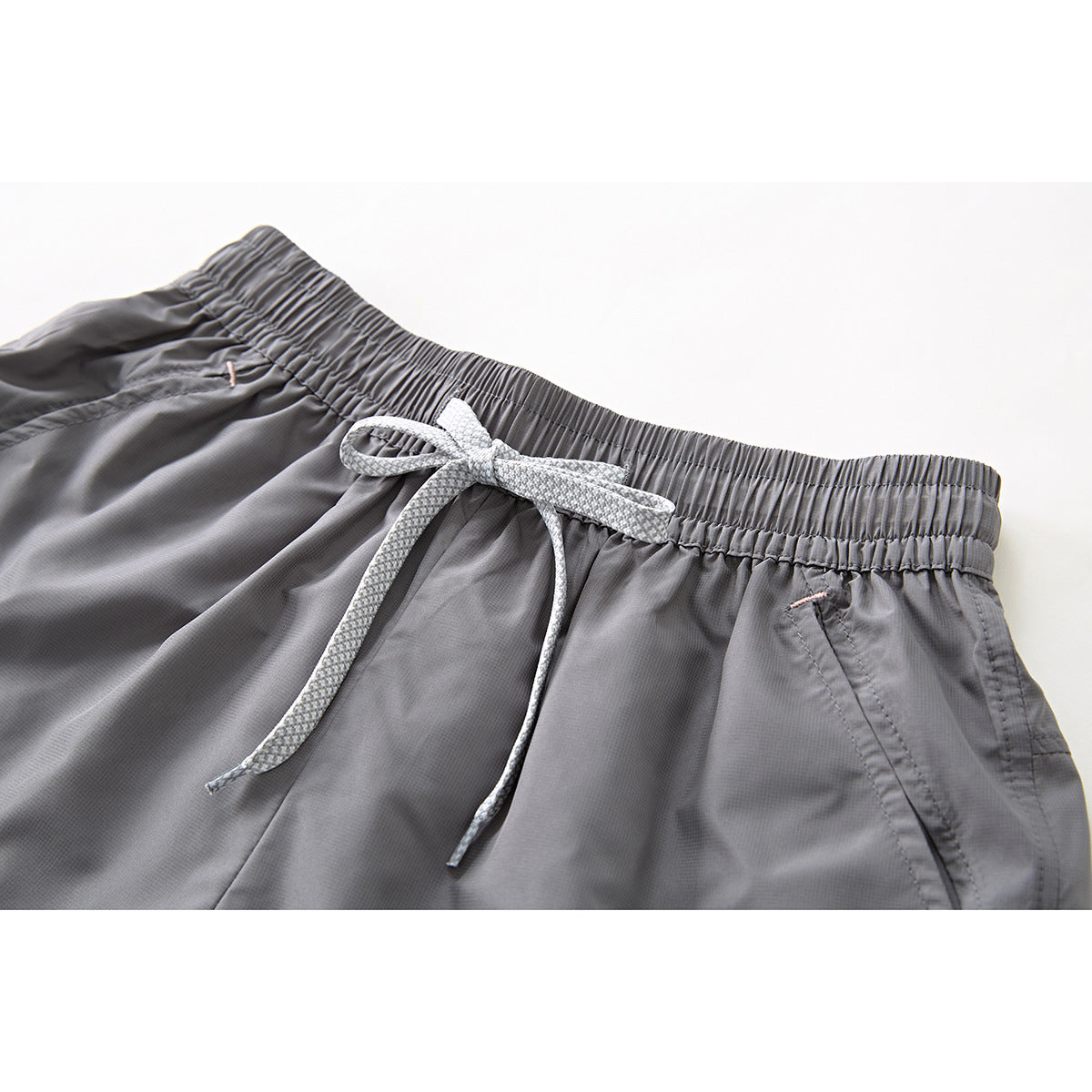 Close-up of gray shorts with a gathered elastic waistband, white drawstring, and angled pocket opening.