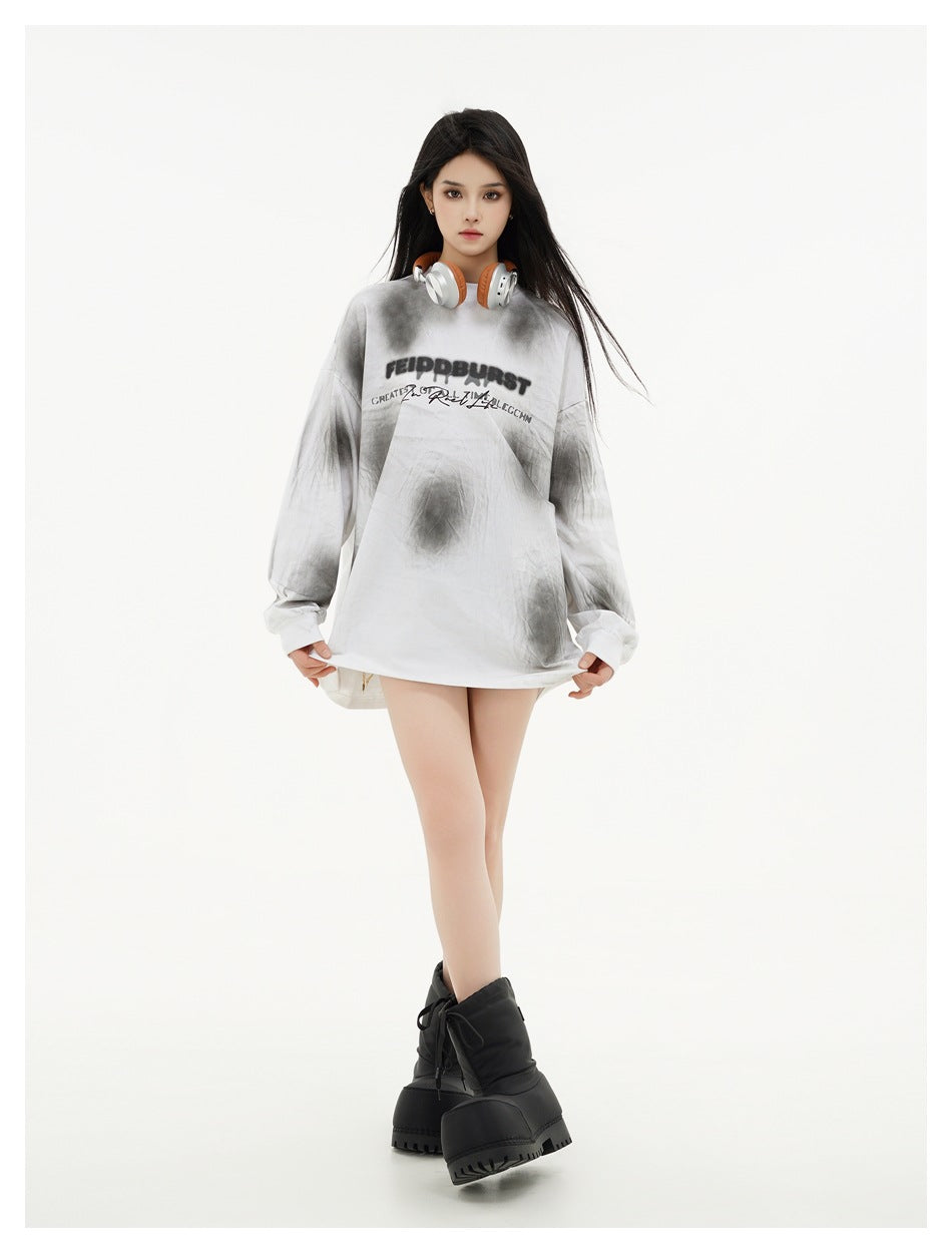 Full-length model wearing an oversized white and gray tie-dye shirt with black chest lettering and black boots.