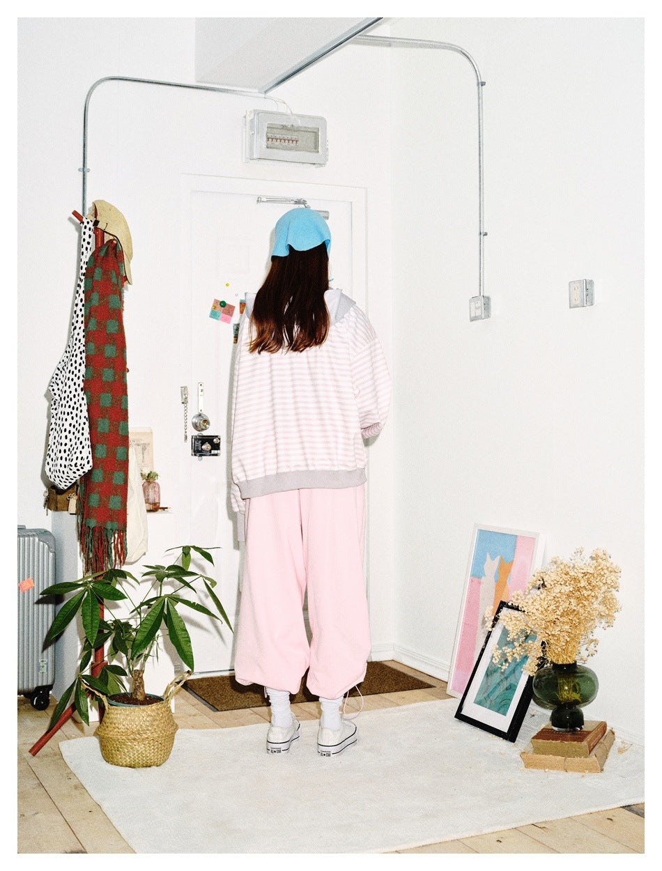 Back view of a model wearing a pale pink-and-white striped zip hoodie with gray trim and loose pink pants.