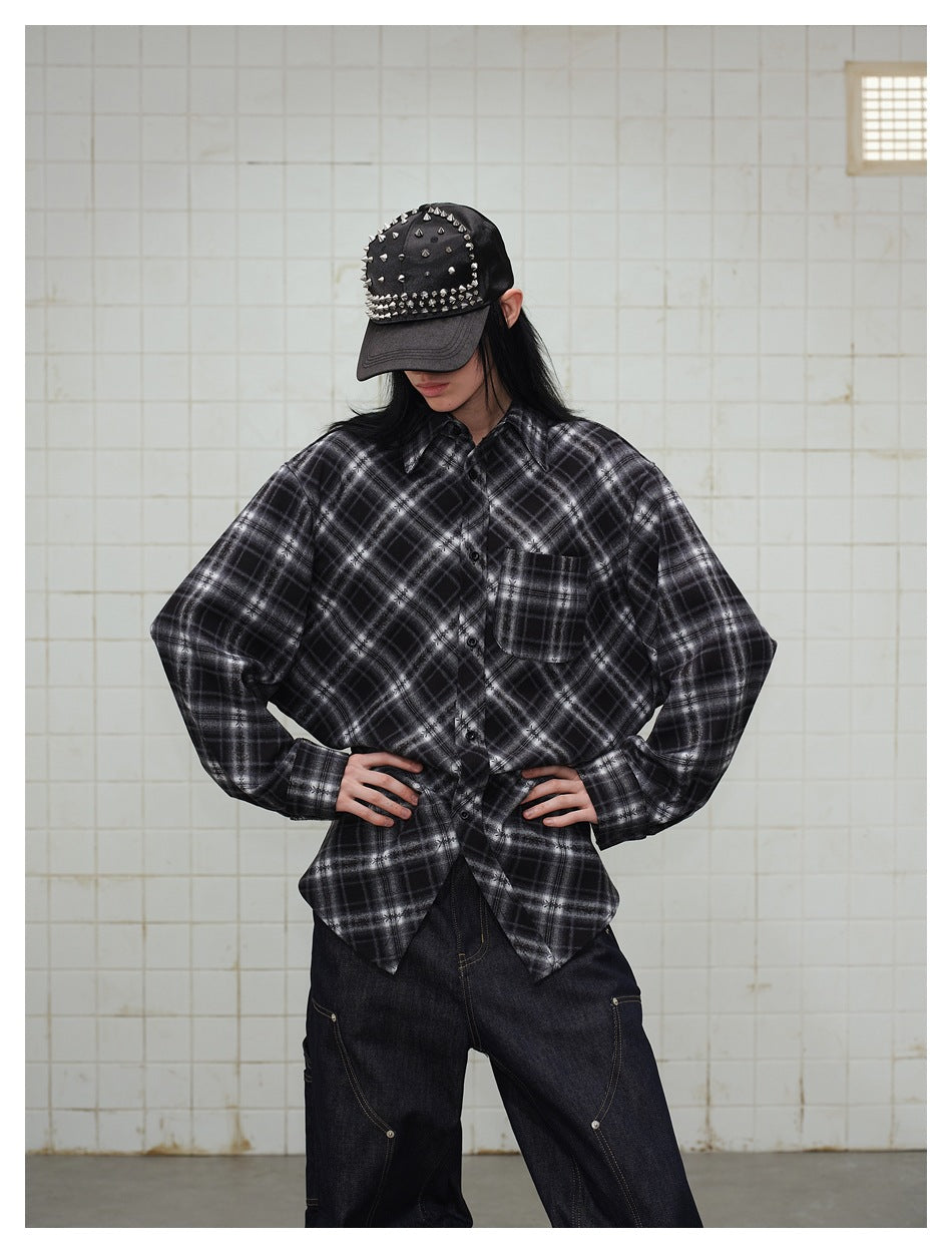 Model wearing an oversized black and gray plaid button-up shirt with a chest pocket and a studded black cap.