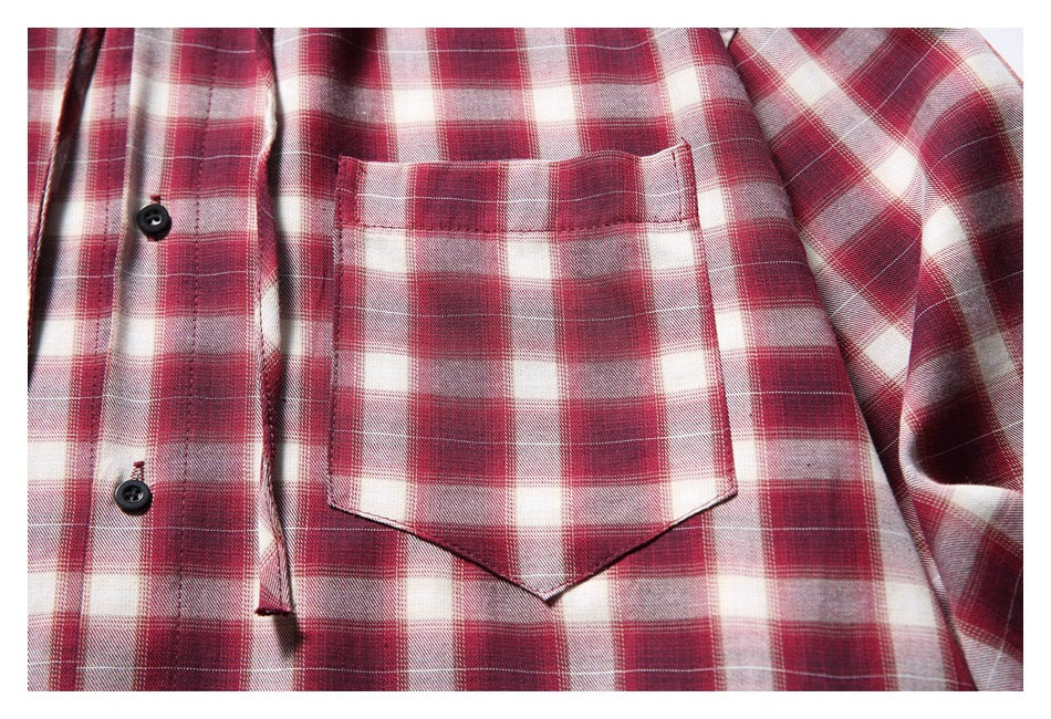 Close-up of a red, burgundy, and cream plaid shirt with a pointed chest pocket and black buttons.
