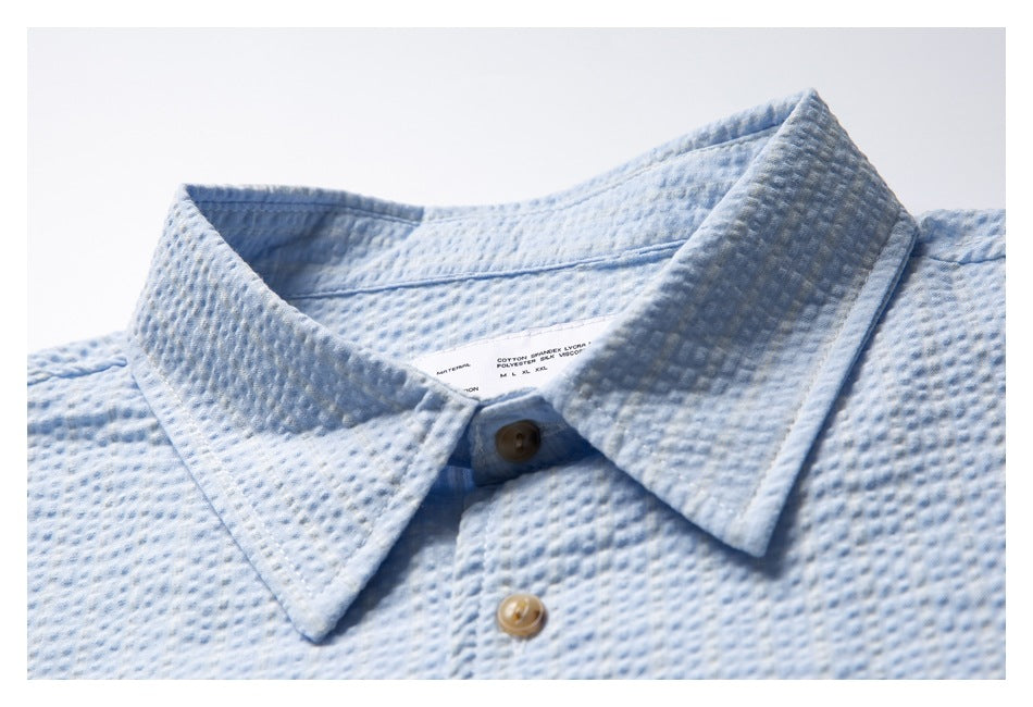 Close-up of a pale blue textured shirt collar, button placket, and interior care label.
