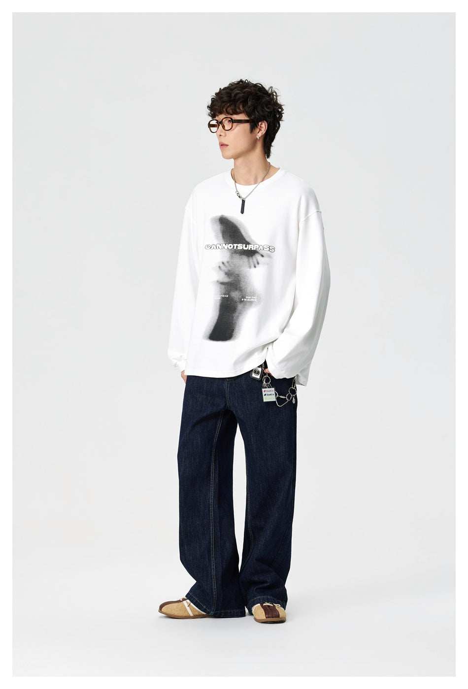 Side view of a model wearing a white long-sleeve graphic shirt with dark wide-leg jeans.