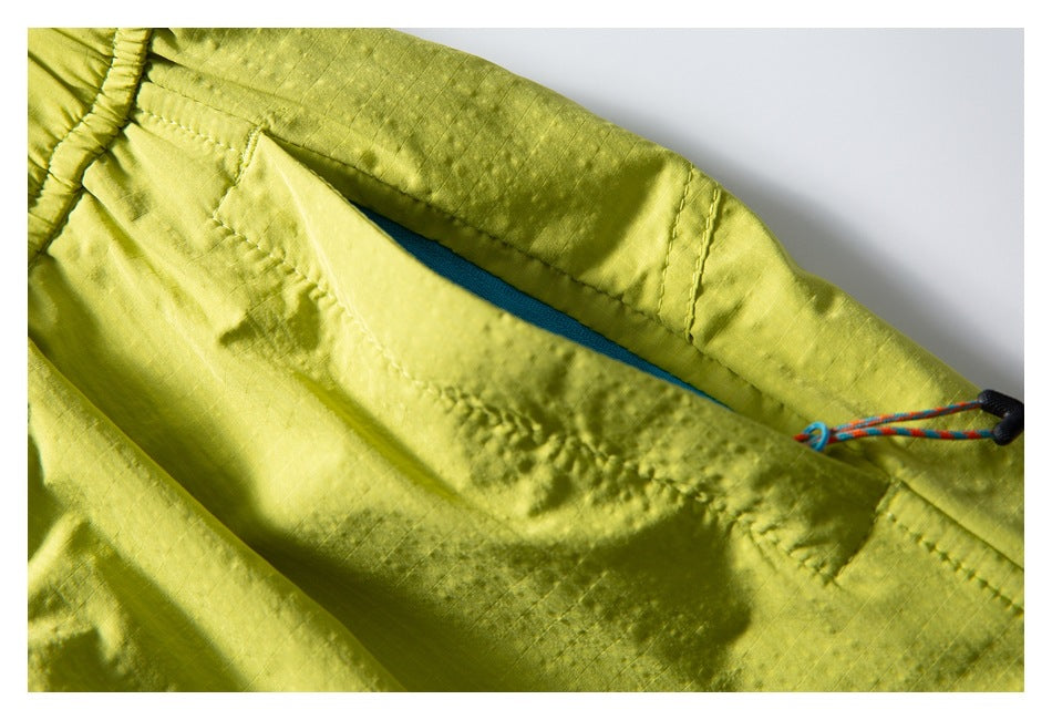 Close-up of lime-yellow shorts showing a pocket opening with teal edging and a multicolored cord with black toggle.