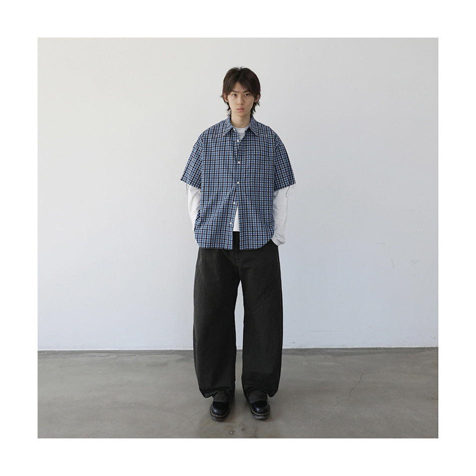 Model wearing the blue plaid short-sleeve shirt open over a white long-sleeve top with dark wide-leg pants and black boots