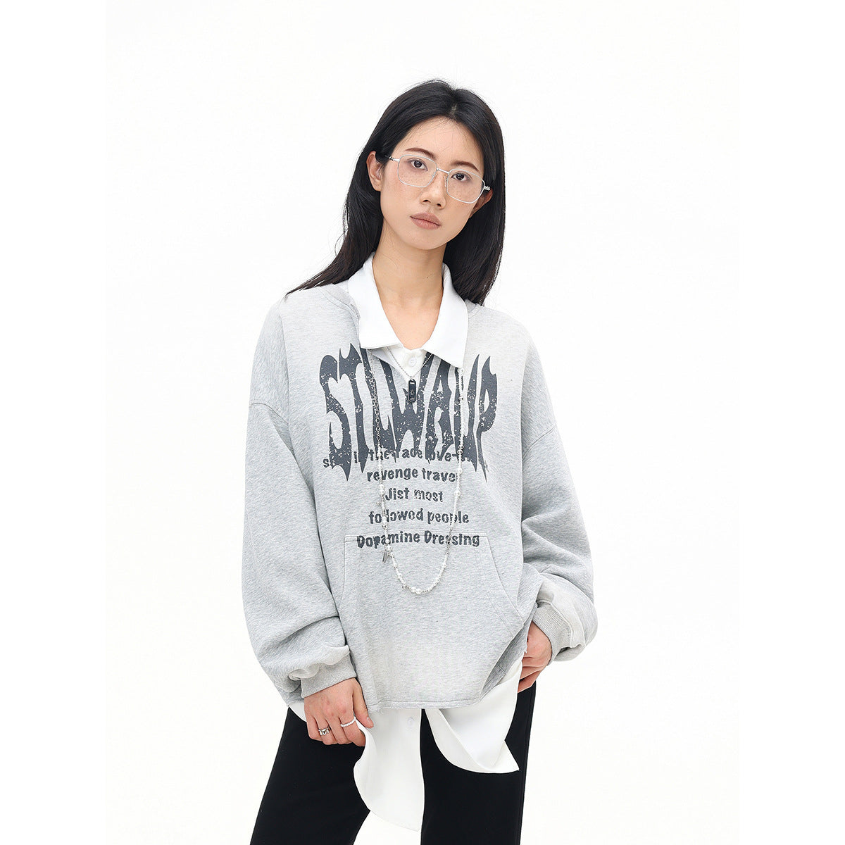 Model wearing a light gray sweatshirt with a large black chest graphic, white collar, and layered shirt hem.