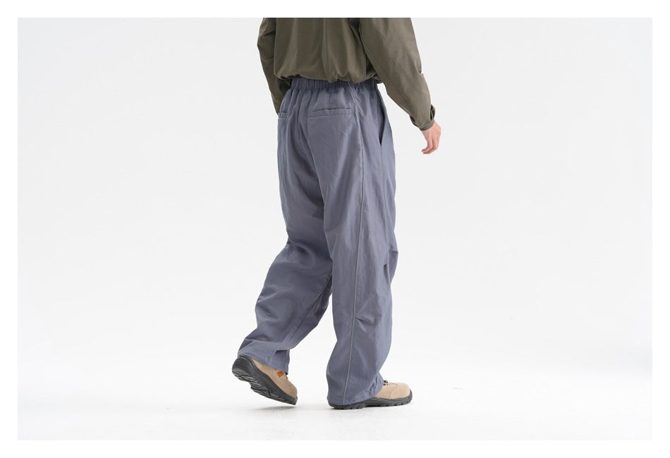 Rear view of a model wearing loose slate-blue trousers with an elastic waist and back pocket.