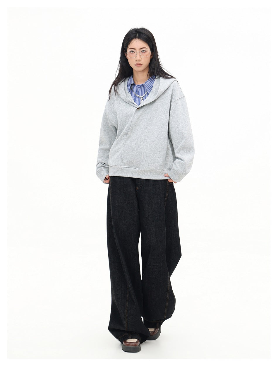 Model wearing an oversized light gray hooded sweatshirt with a buttoned crossover neckline and wide black jeans.