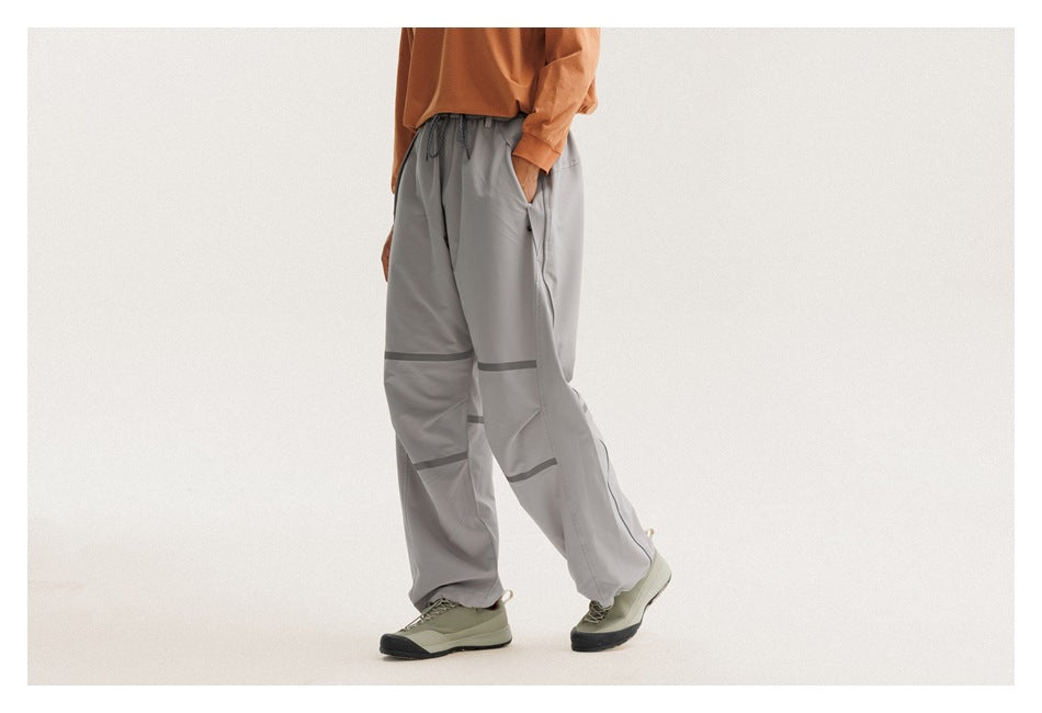 Angled view of a model wearing loose light-gray drawstring pants with dark bands across the legs.