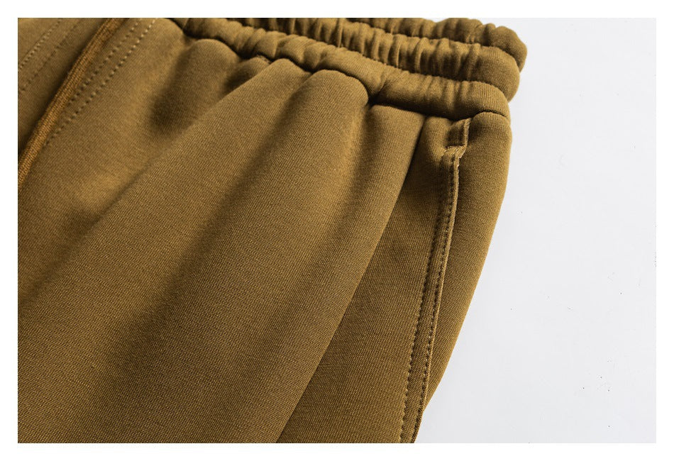 Close-up of ochre joggers showing the elastic waistband and stitched side pocket seam.