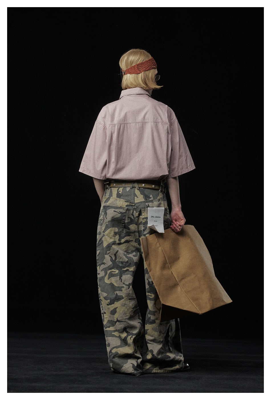 Rear view of a model wearing a dusty pink short-sleeve shirt and loose camouflage pants.