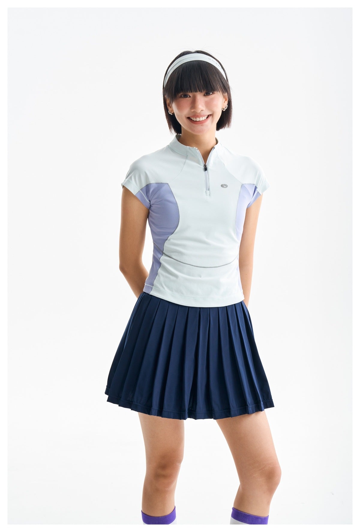 Closer view of a woman wearing a pale blue quarter-zip top with lavender side panels and a navy pleated skirt.