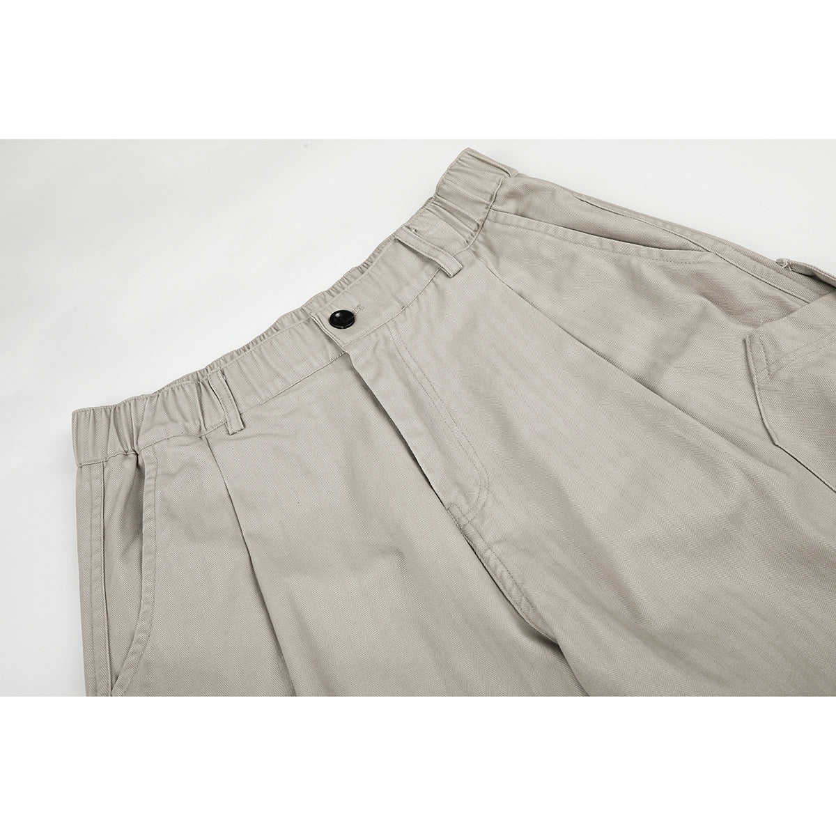 Close-up of light greige trousers showing the elasticized waistband, belt loops, black button, and front fly.