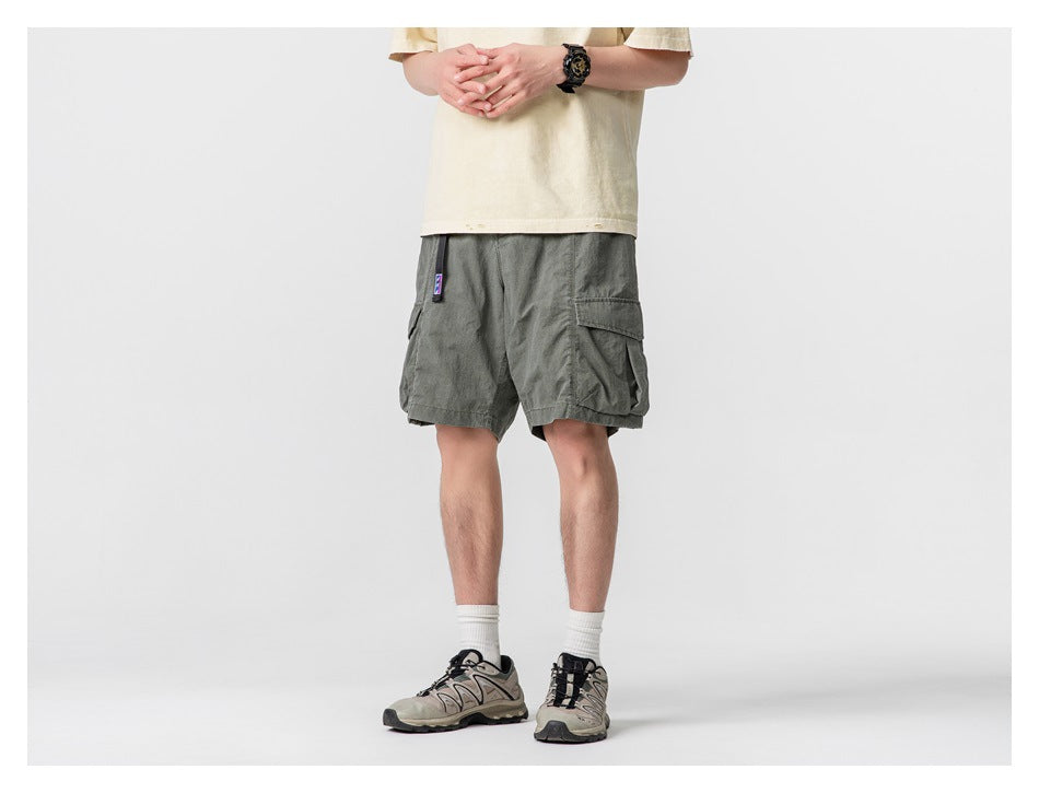Front three-quarter view of dark gray-green cargo shorts with prominent side pockets, worn by a model.
