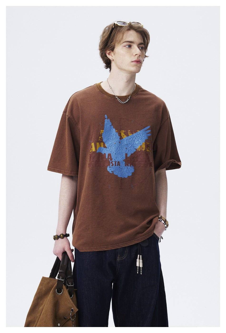 Model wearing a brown oversized T-shirt with a blue eagle graphic, shown from the front with dark jeans.