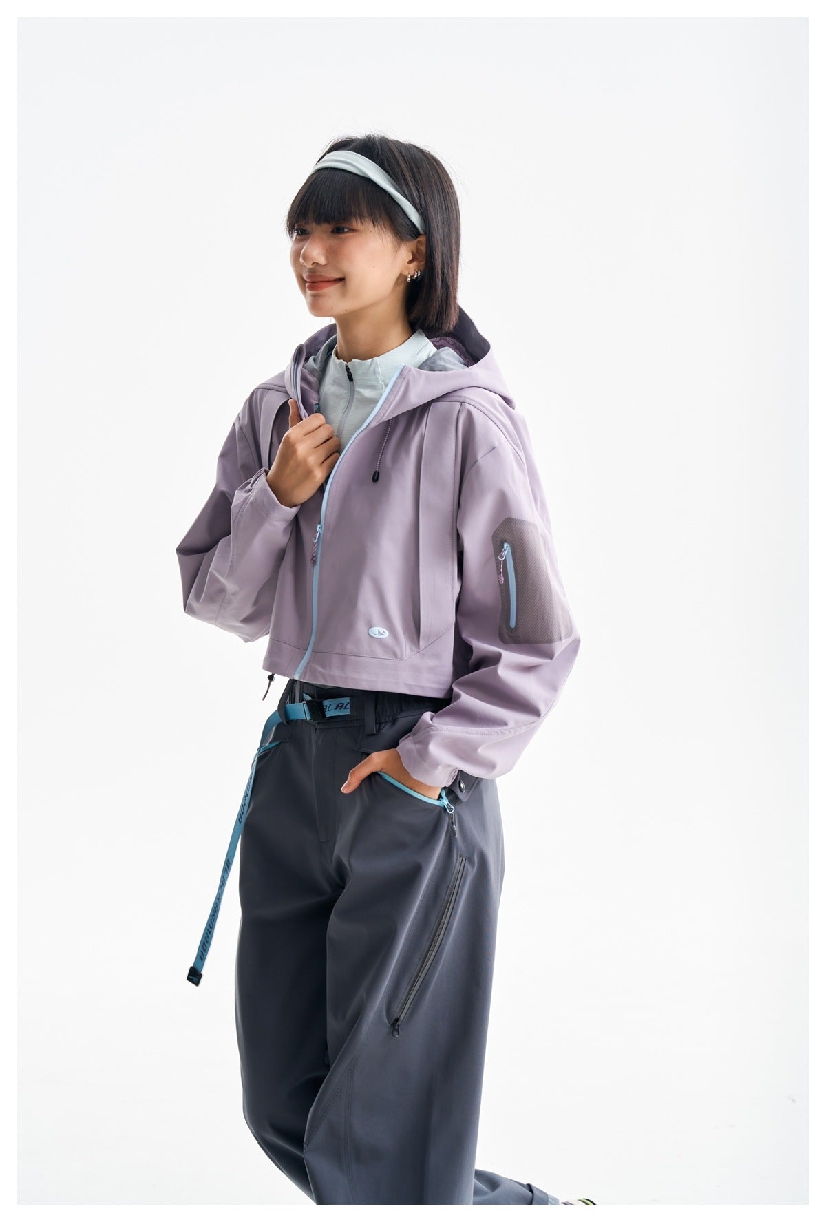 Model wearing a cropped lavender hooded jacket with light blue trim and loose charcoal pants.