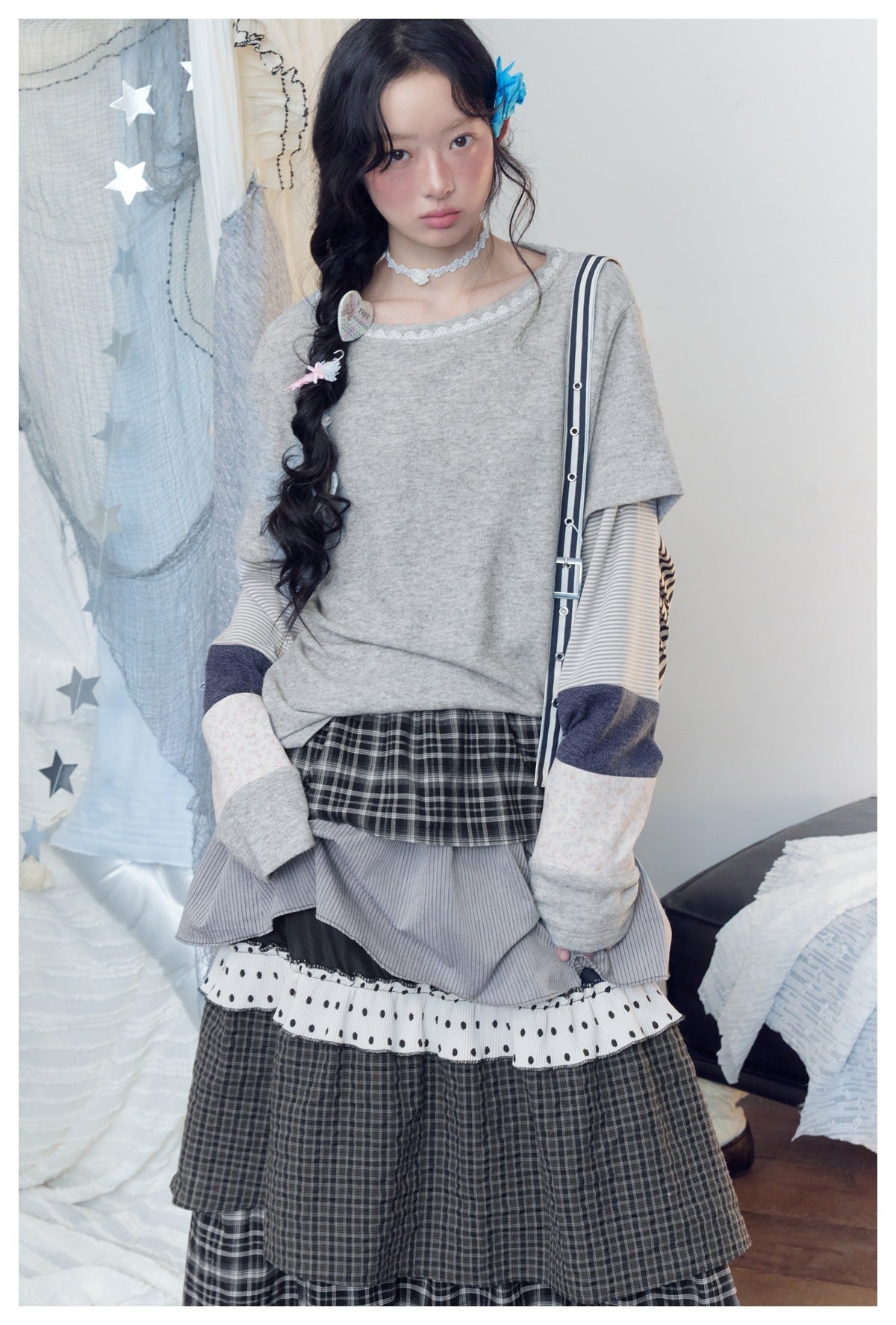 Model in a gray lace-trim top with striped, navy, and floral sleeve panels and a tiered plaid skirt.