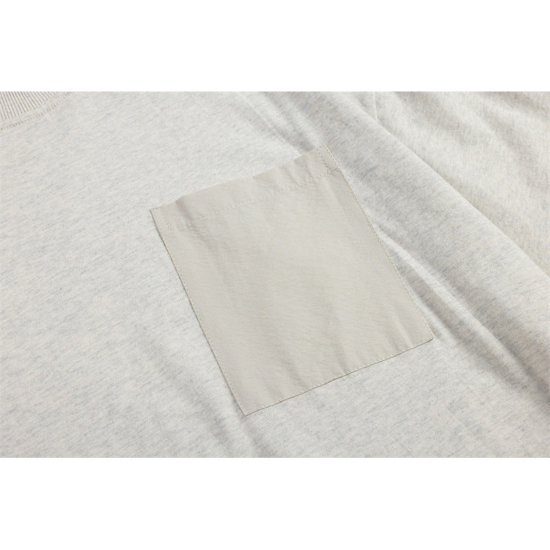 Close-up of a square light-colored patch pocket on a light heather gray T-shirt.