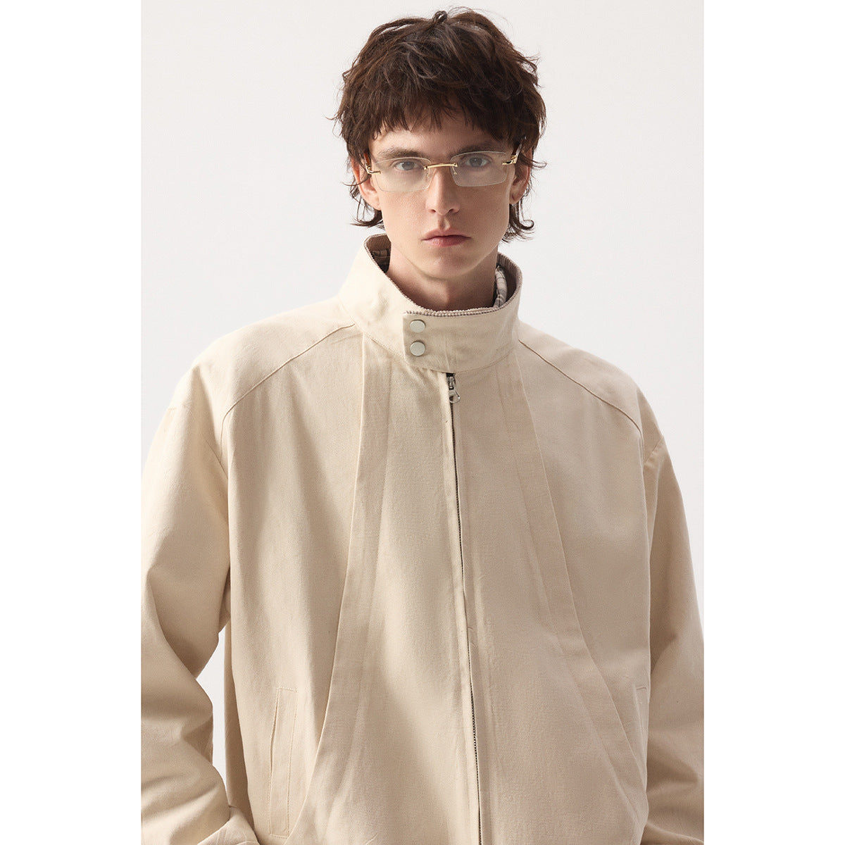 Close view of a model wearing a light beige jacket with a high snap collar, center zipper, and angled seams.