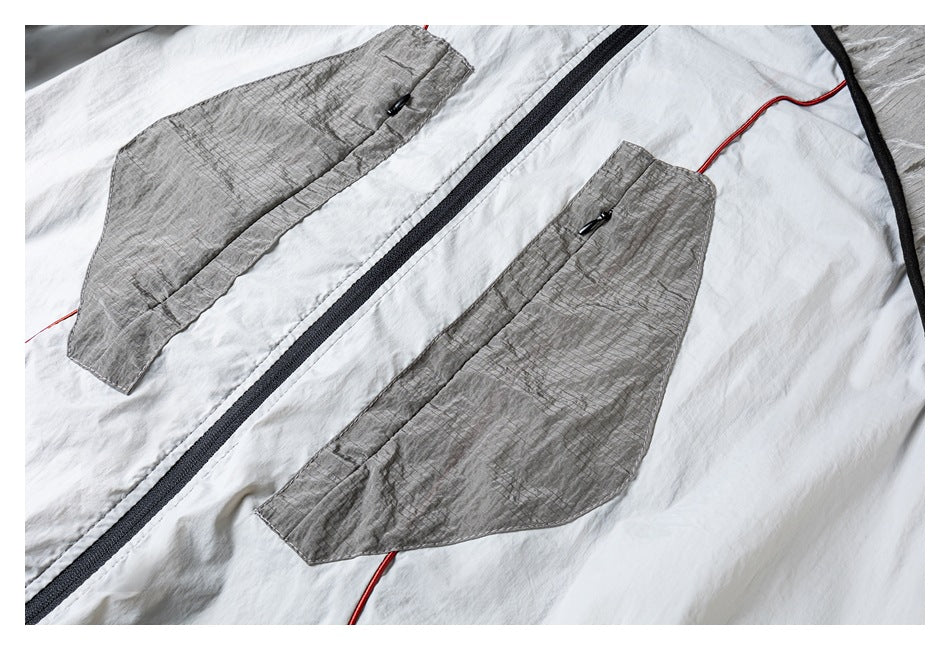 Close-up of two angular gray front pockets, black center zipper, and red piping on the light jacket.