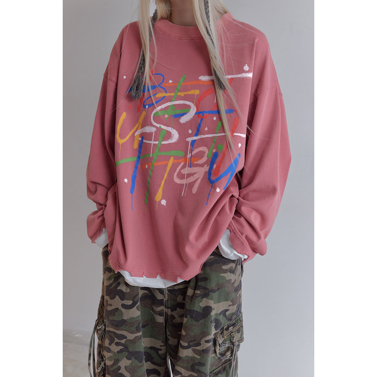 Close view of a dusty rose oversized sweatshirt with colorful abstract lettering and a layered white hem.