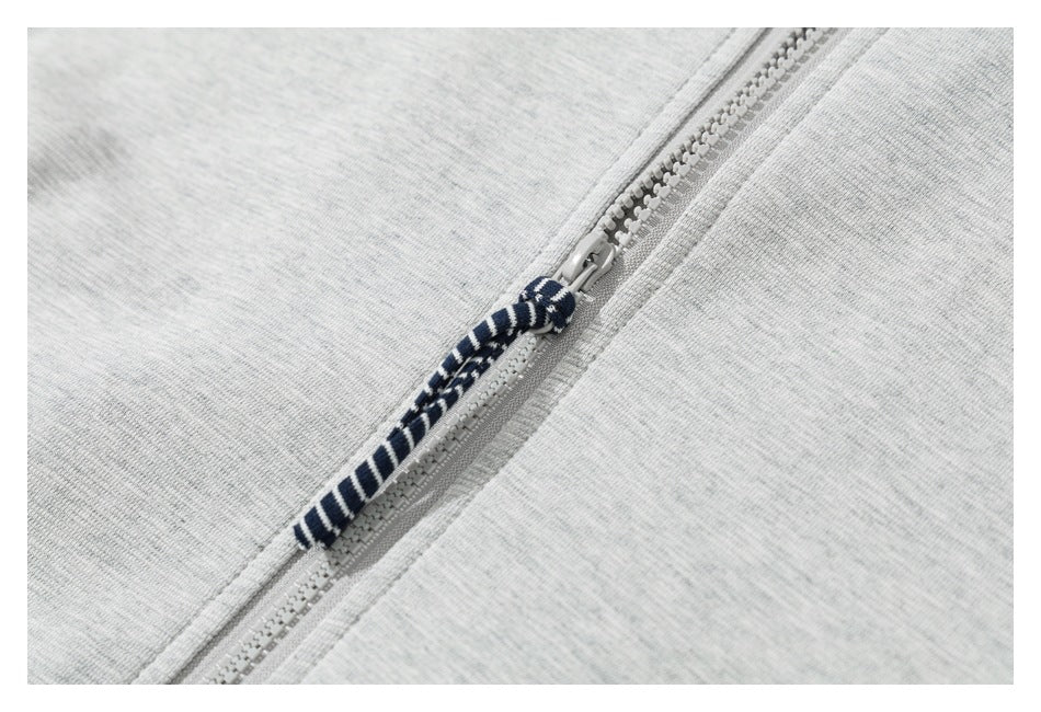 Close-up of a light gray jogger zipper with a navy-and-white striped fabric pull.