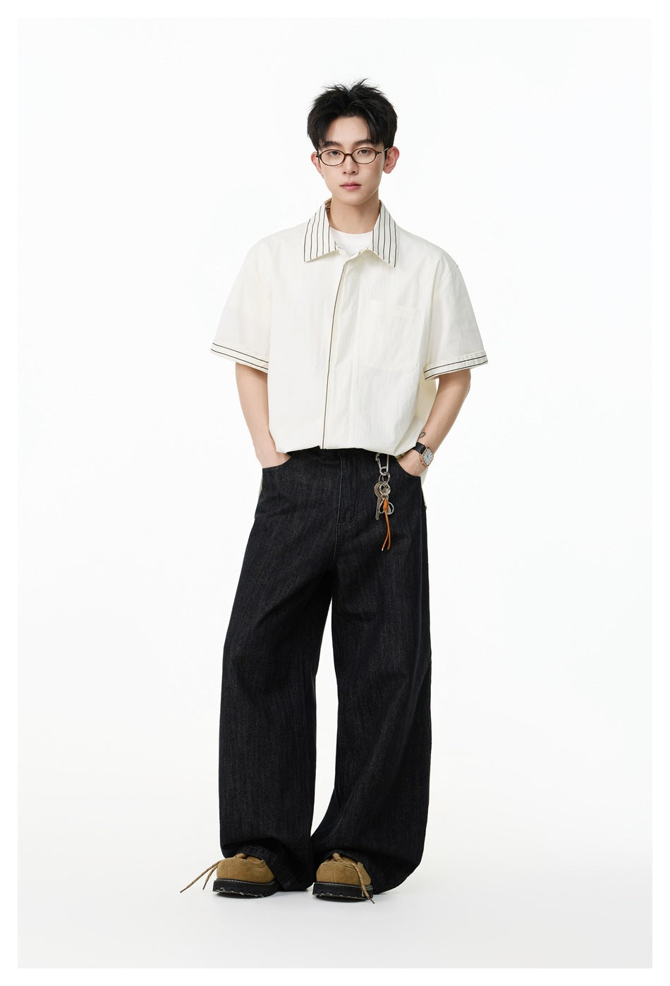 Model wearing an ivory short-sleeve shirt with striped collar and cuffs, paired with loose black jeans.