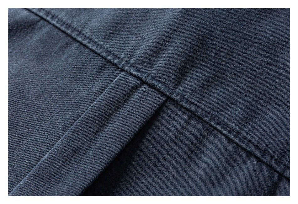 Close-up of dark blue denim showing a diagonal stitched seam and overlapping fabric folds.